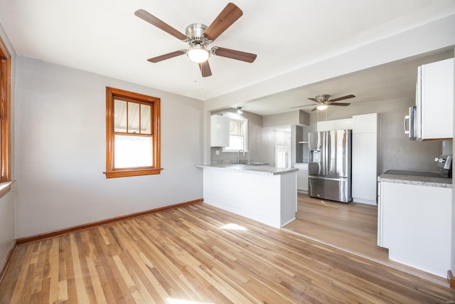 kitchen with light wood finished floors, appliances with stainless steel finishes, white cabinetry, a sink, and a peninsula