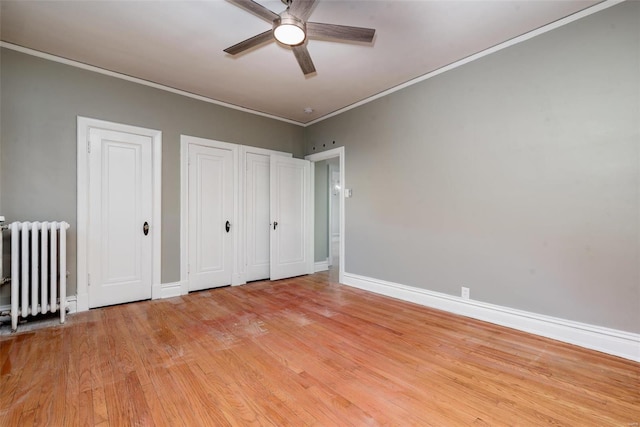 unfurnished bedroom with ornamental molding, light wood-type flooring, two closets, radiator heating unit, and ceiling fan