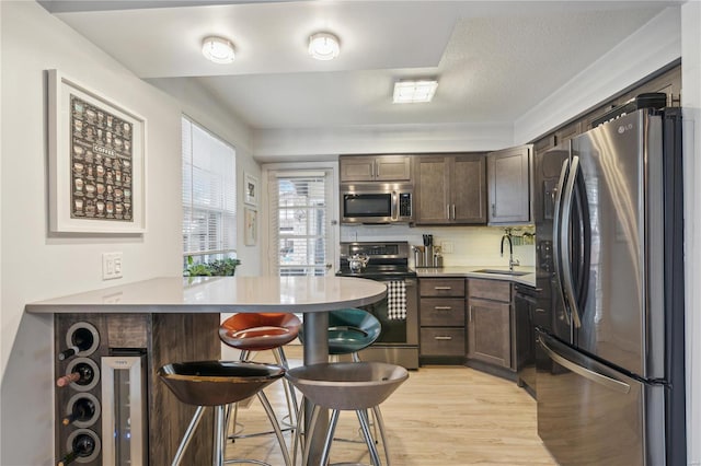 kitchen with sink, a breakfast bar area, appliances with stainless steel finishes, light hardwood / wood-style floors, and kitchen peninsula