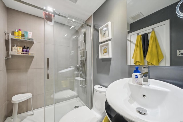 bathroom featuring a shower with door, sink, and toilet