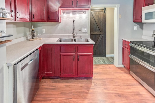 kitchen with appliances with stainless steel finishes, a barn door, light hardwood / wood-style floors, and sink