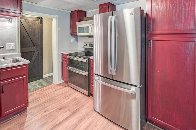 kitchen with appliances with stainless steel finishes, a barn door, sink, and light hardwood / wood-style flooring