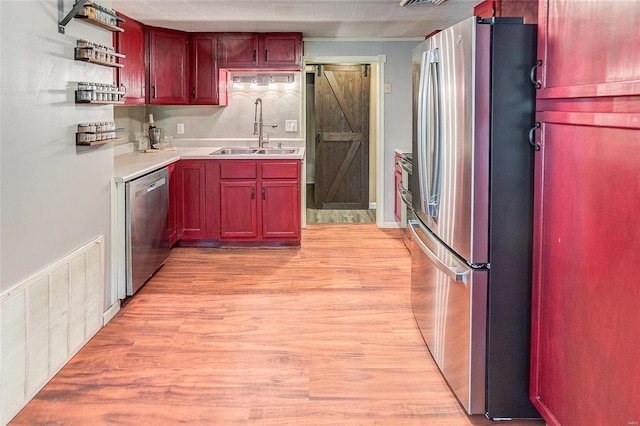 kitchen with a barn door, light wood-type flooring, appliances with stainless steel finishes, and sink