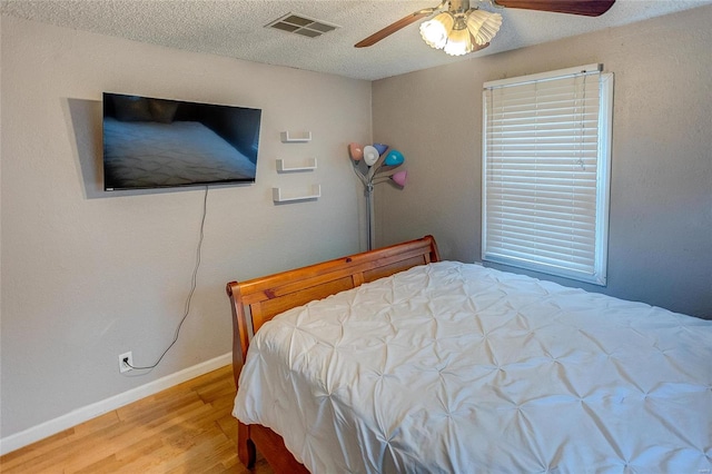 bedroom with hardwood / wood-style floors, ceiling fan, and a textured ceiling