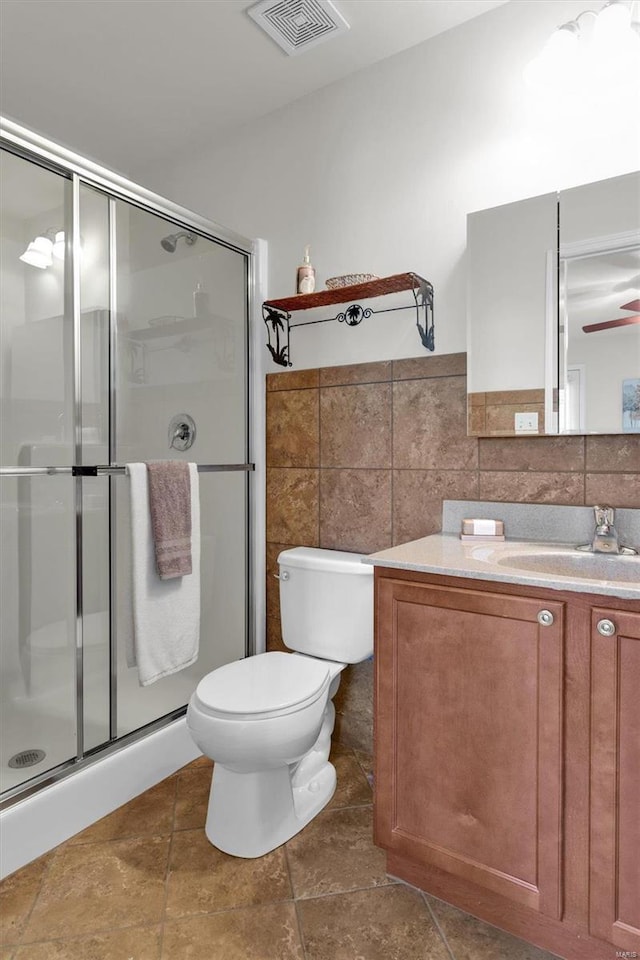 bathroom with vanity, a shower with door, ceiling fan, toilet, and tile walls