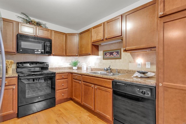 kitchen with light stone countertops, decorative backsplash, sink, black appliances, and light hardwood / wood-style floors