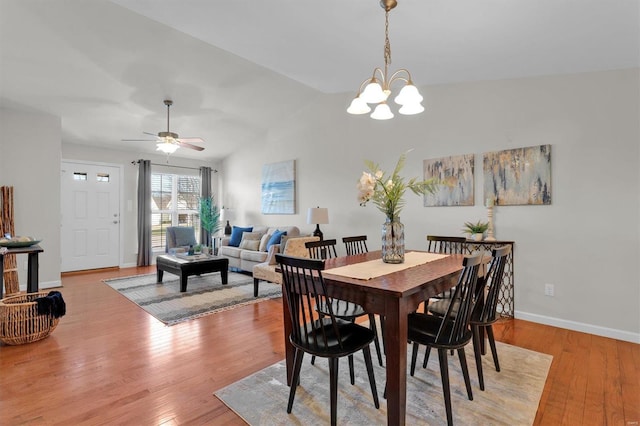 dining area featuring ceiling fan with notable chandelier, light hardwood / wood-style floors, and vaulted ceiling