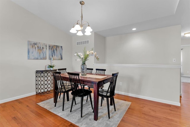 dining space with a notable chandelier, lofted ceiling, and light hardwood / wood-style flooring