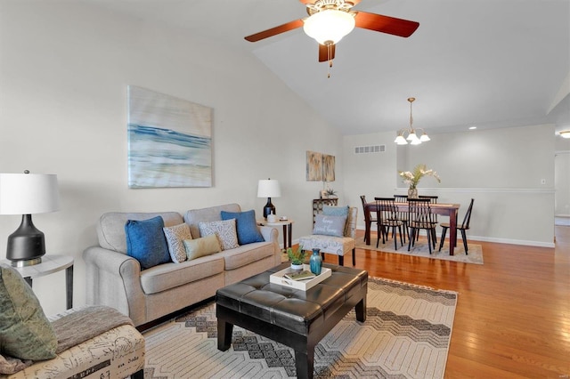 living room featuring light hardwood / wood-style flooring, ceiling fan with notable chandelier, and vaulted ceiling