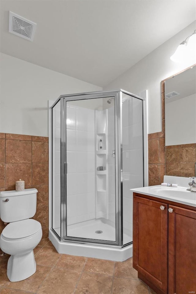 bathroom with vanity, a shower with door, tile patterned floors, toilet, and tile walls