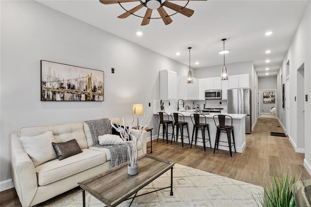 living room featuring light wood-type flooring, ceiling fan, and sink