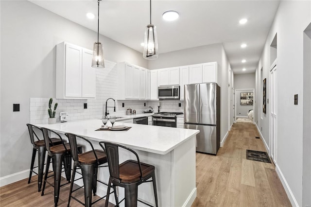 kitchen featuring stainless steel appliances, white cabinetry, a kitchen breakfast bar, light hardwood / wood-style floors, and kitchen peninsula