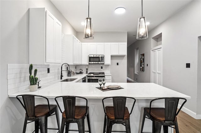 kitchen featuring white cabinetry, appliances with stainless steel finishes, a kitchen bar, sink, and kitchen peninsula