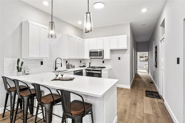 kitchen featuring a kitchen bar, stainless steel appliances, white cabinets, kitchen peninsula, and light hardwood / wood-style flooring