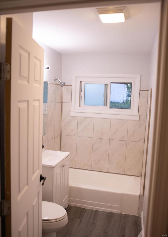 full bathroom featuring wood-type flooring, toilet, tile walls, vanity, and tiled shower / bath combo