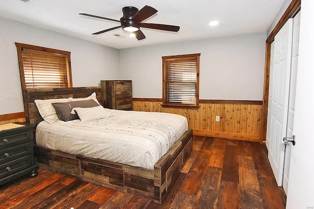 bedroom with a closet, wood walls, ceiling fan, and dark hardwood / wood-style flooring