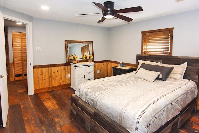 bedroom with dark hardwood / wood-style floors, a barn door, wooden walls, and ceiling fan