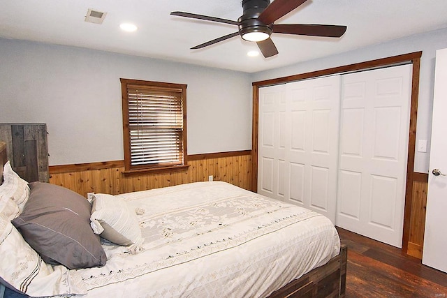 bedroom featuring a closet, dark hardwood / wood-style floors, wood walls, and ceiling fan