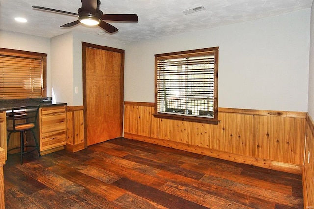 unfurnished office with wood walls, dark wood-type flooring, a textured ceiling, and ceiling fan