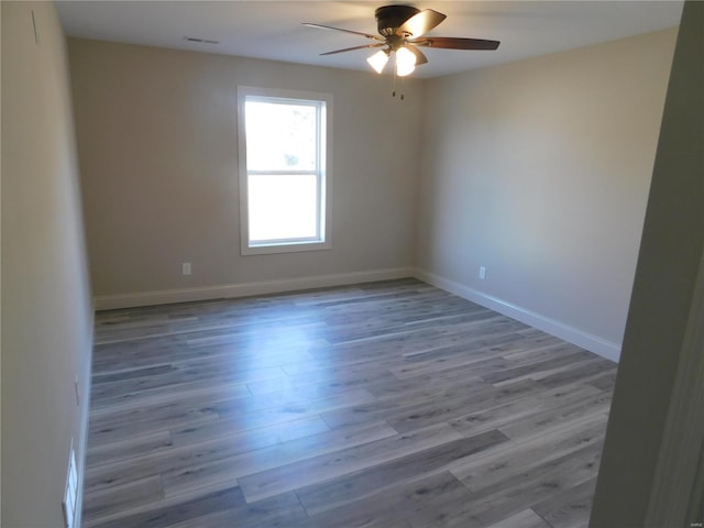 spare room with a ceiling fan, visible vents, baseboards, and wood finished floors