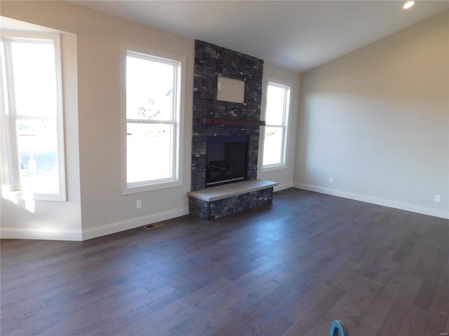 unfurnished living room with a healthy amount of sunlight, dark wood-style floors, a large fireplace, and lofted ceiling