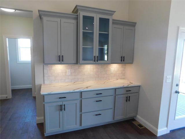 kitchen with glass insert cabinets, dark wood-style flooring, light stone countertops, gray cabinets, and backsplash