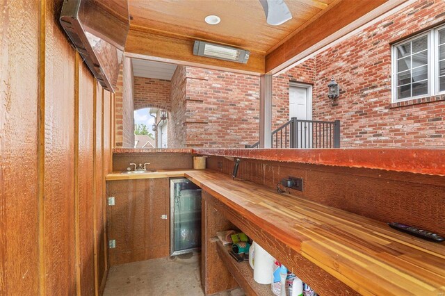 bar with beverage cooler, concrete flooring, brick wall, and sink