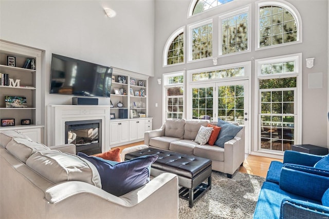 living room with light hardwood / wood-style flooring, built in features, and a high ceiling