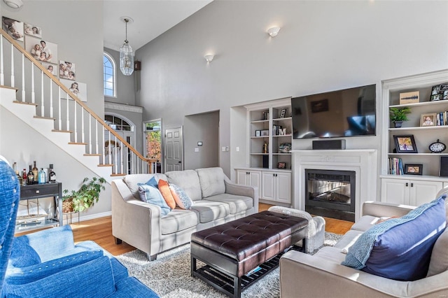 living room featuring high vaulted ceiling, light hardwood / wood-style flooring, and built in shelves