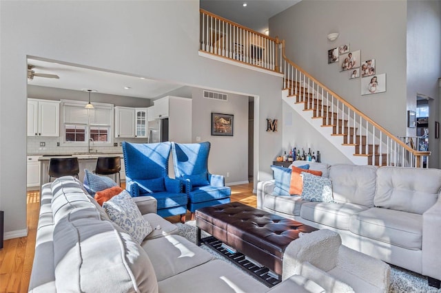 living room featuring a towering ceiling, sink, and light hardwood / wood-style floors