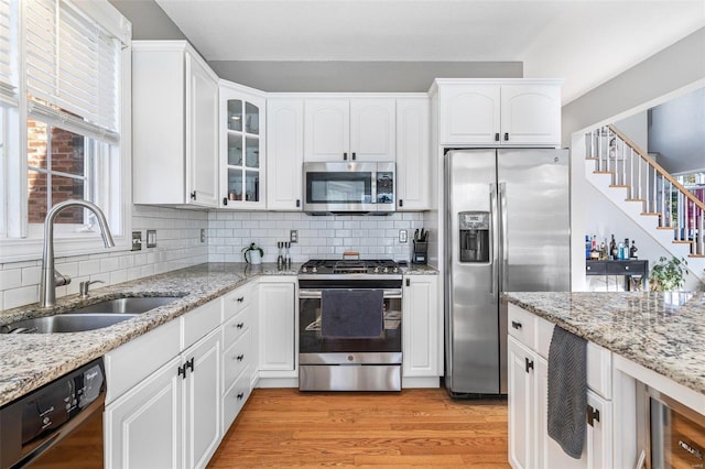 kitchen with sink, light wood-type flooring, backsplash, white cabinetry, and stainless steel appliances