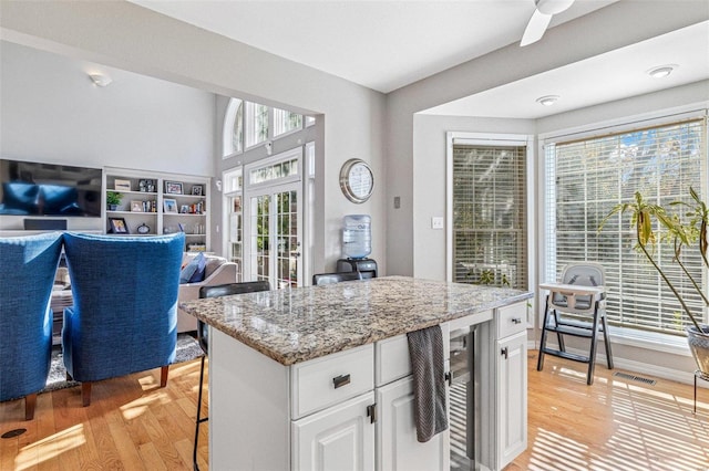 kitchen featuring white cabinets, wine cooler, ceiling fan, light stone countertops, and light hardwood / wood-style floors