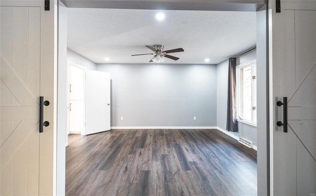 spare room featuring a textured ceiling, a barn door, dark wood-type flooring, and ceiling fan