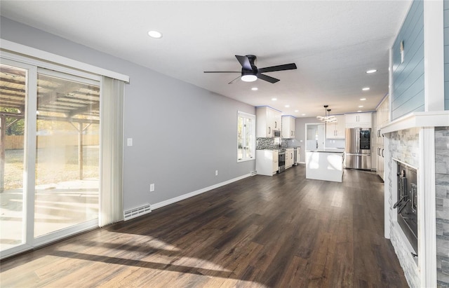 unfurnished living room with ceiling fan, a stone fireplace, and dark hardwood / wood-style flooring