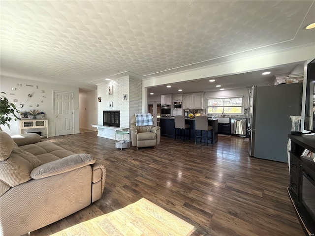 living room with dark wood-type flooring, a fireplace, a textured ceiling, and ornamental molding