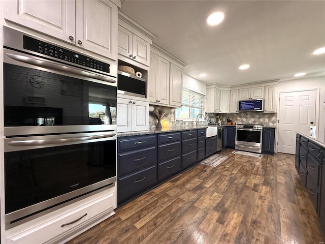 kitchen with light stone countertops, appliances with stainless steel finishes, white cabinetry, tasteful backsplash, and dark hardwood / wood-style floors