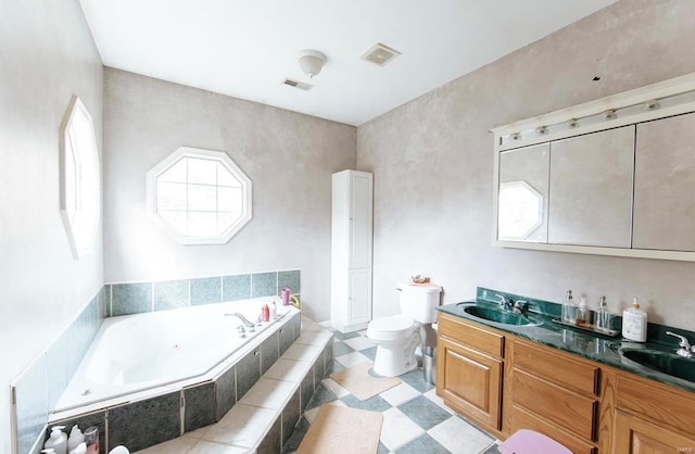 bathroom with toilet, vanity, and tiled bath