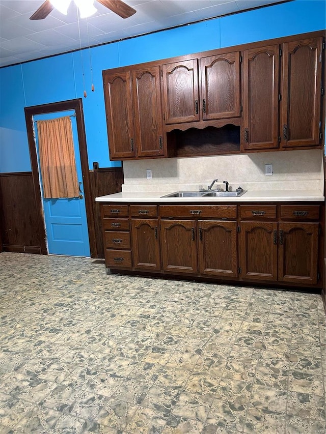 kitchen featuring wooden walls, sink, dark brown cabinets, and ceiling fan