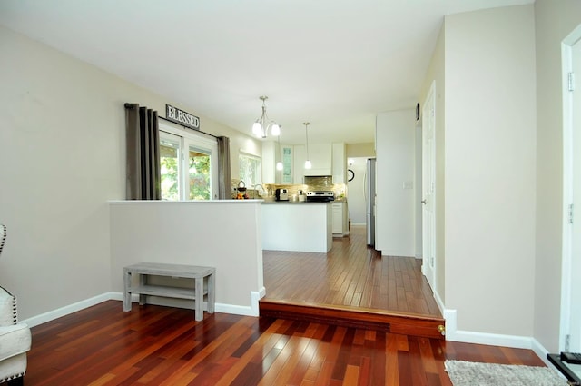 kitchen with kitchen peninsula, decorative backsplash, white cabinets, hanging light fixtures, and dark wood-type flooring