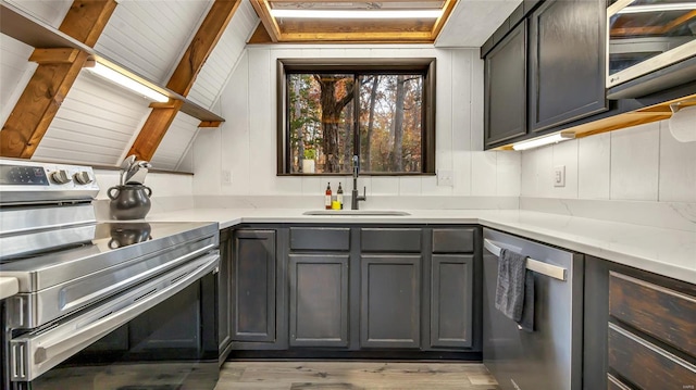 kitchen with appliances with stainless steel finishes, light stone countertops, vaulted ceiling with beams, gray cabinets, and sink