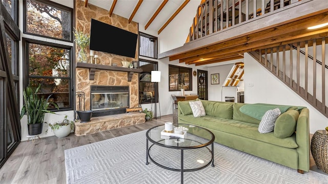 living room featuring beam ceiling, a stone fireplace, hardwood / wood-style flooring, and high vaulted ceiling