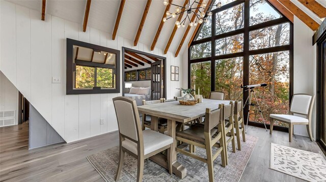 dining area with wood walls, hardwood / wood-style floors, beam ceiling, high vaulted ceiling, and an inviting chandelier