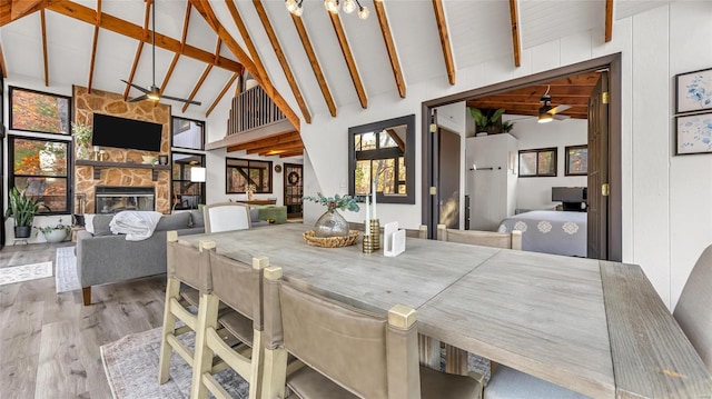 dining area with beam ceiling, a stone fireplace, light wood-type flooring, and high vaulted ceiling