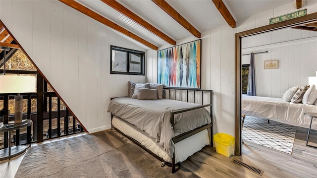 bedroom with hardwood / wood-style floors, lofted ceiling with beams, and wooden walls