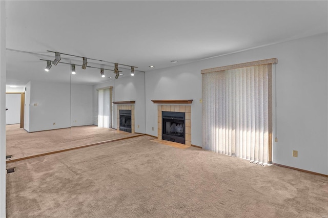 unfurnished living room featuring a tiled fireplace, rail lighting, and light colored carpet