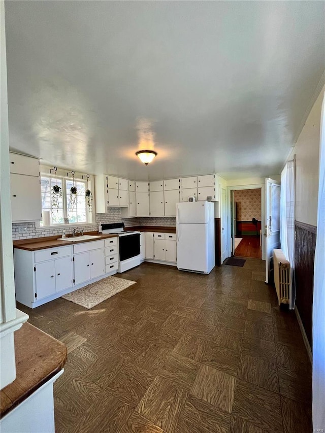 kitchen with radiator heating unit, white appliances, and white cabinetry