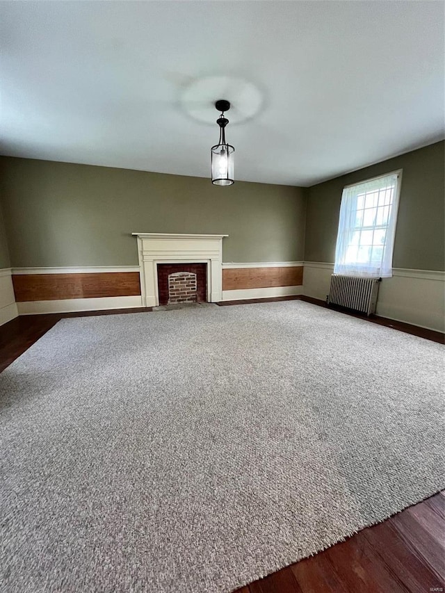 unfurnished living room featuring a fireplace, radiator heating unit, and dark wood-type flooring