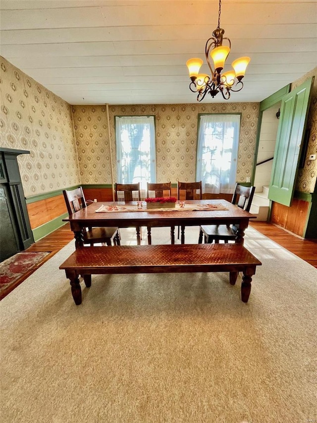 dining area with wood walls, carpet flooring, a healthy amount of sunlight, and a chandelier