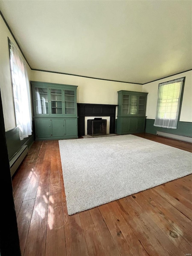 unfurnished living room featuring dark hardwood / wood-style floors, a wealth of natural light, and a baseboard heating unit