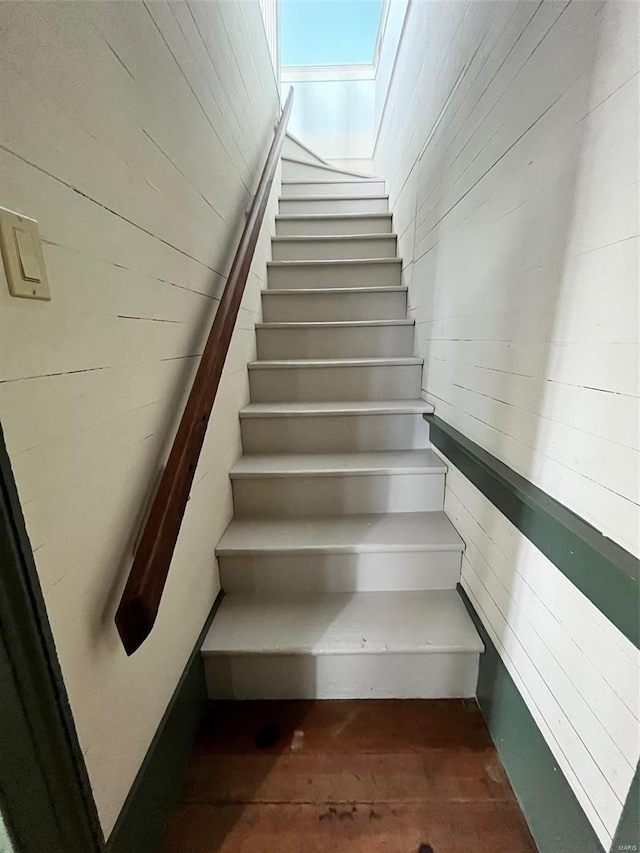 stairway featuring a skylight and wood walls